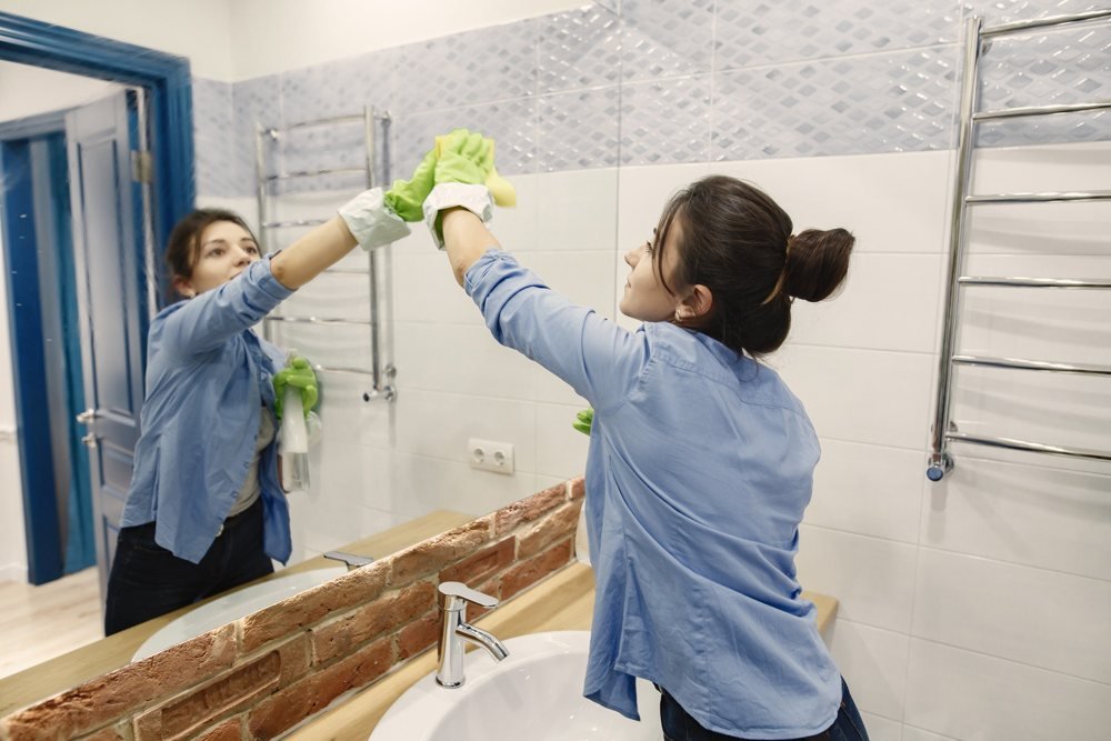 Cleaner polishing a bathroom mirror
