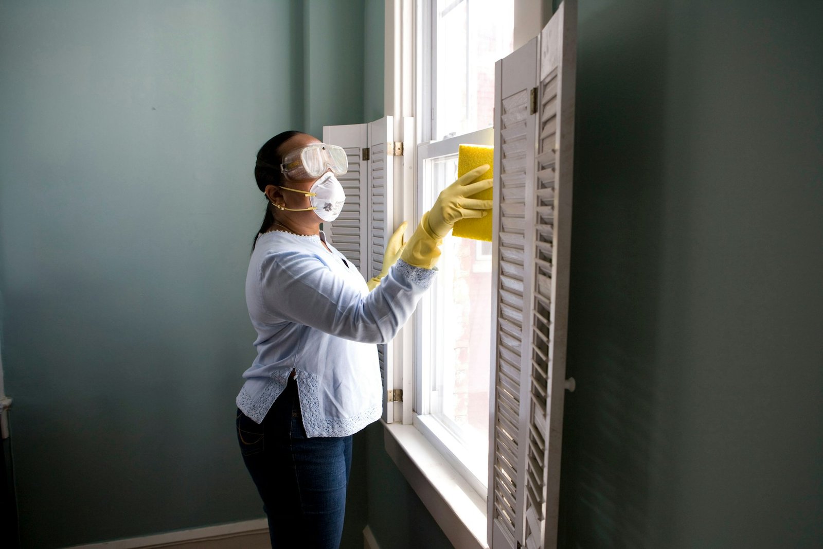 Cleaner wiping a window with gloves and a sponge